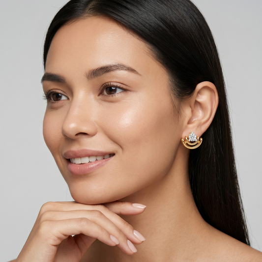 A close-up portrait of a woman wearing a small gold crescent-shaped stud earring with a clear gemstone, set against a clean light gray background.