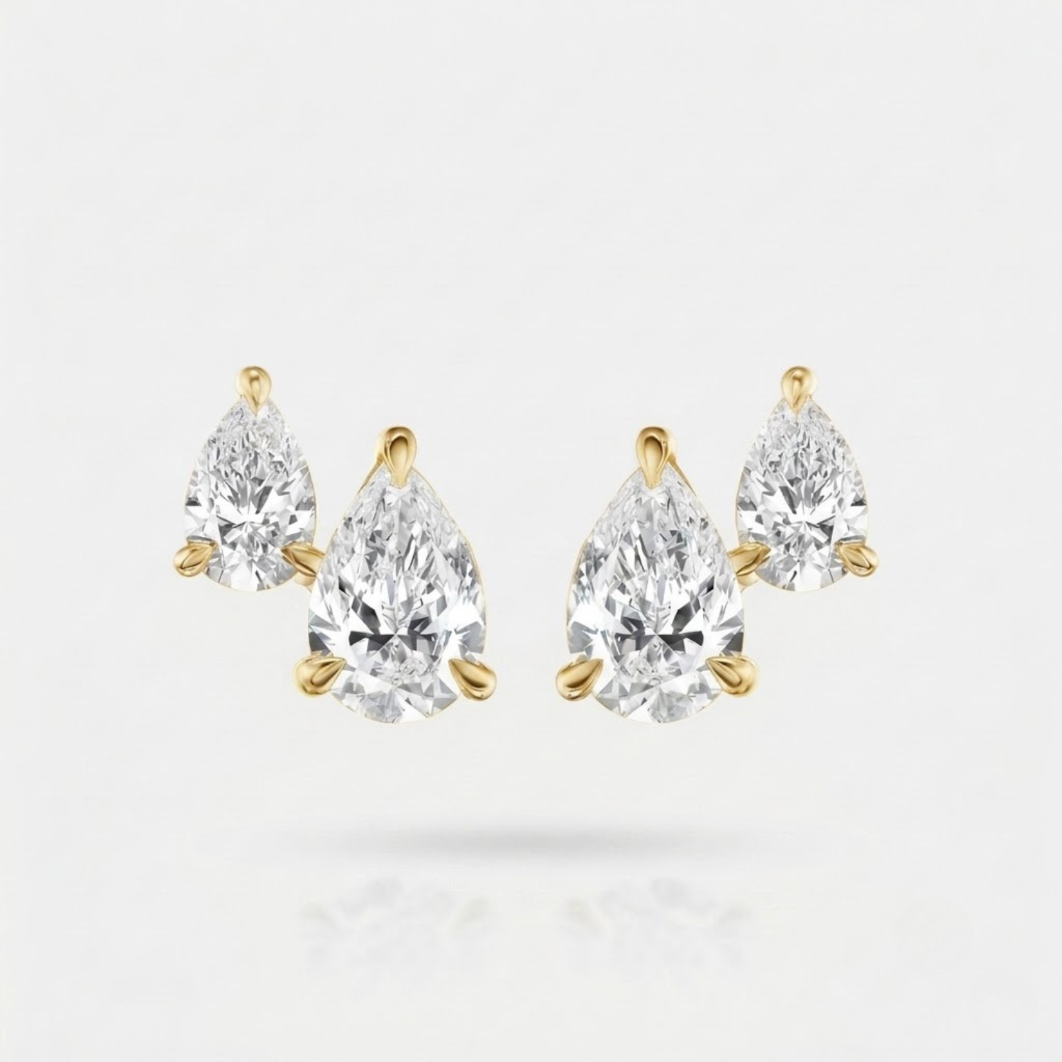 A pair of pear-cut diamond stud earrings in yellow gold settings, displayed on a clean white background with a soft reflection below.
