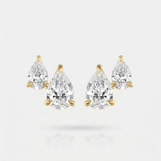 A pair of pear-cut diamond stud earrings in yellow gold settings, displayed on a clean white background with a soft reflection below.