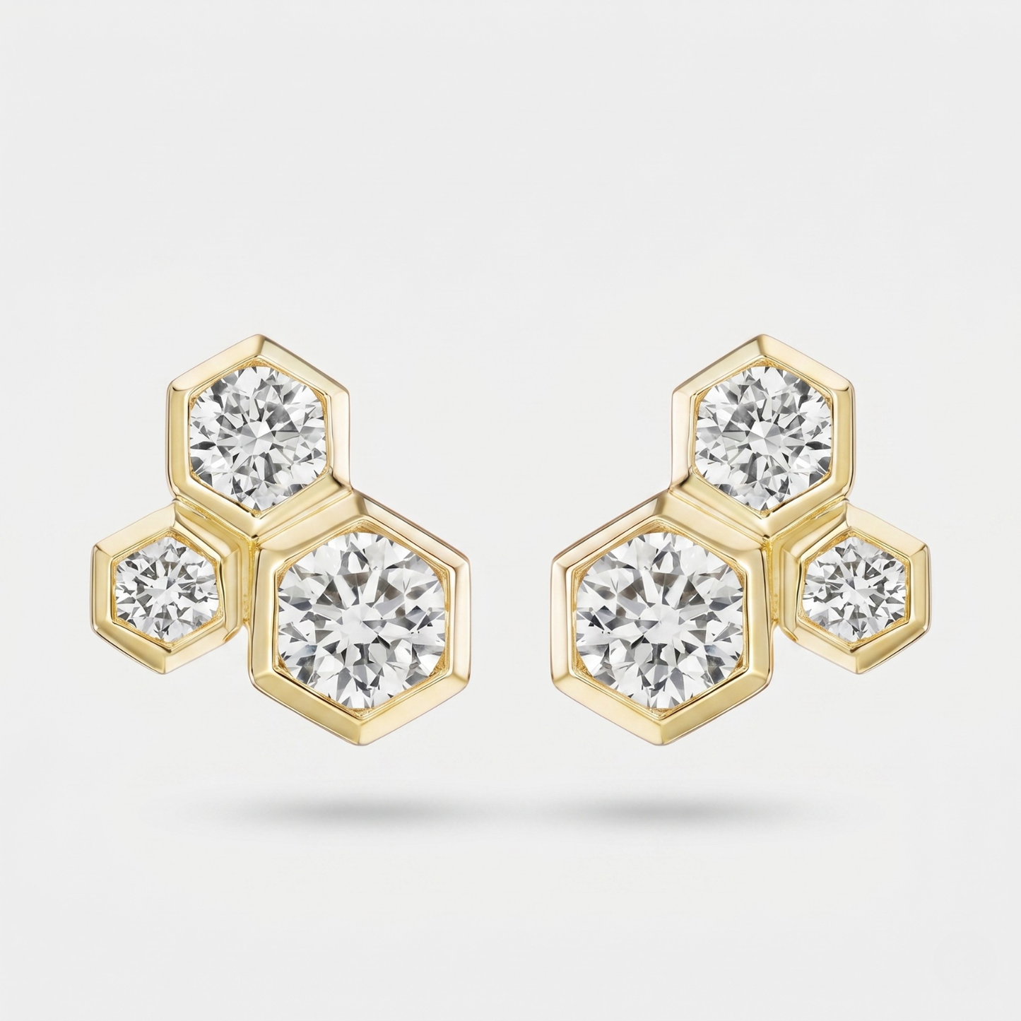 A pair of gold hexagonal stud earrings with round-cut clear gemstones, displayed on a light gray background.