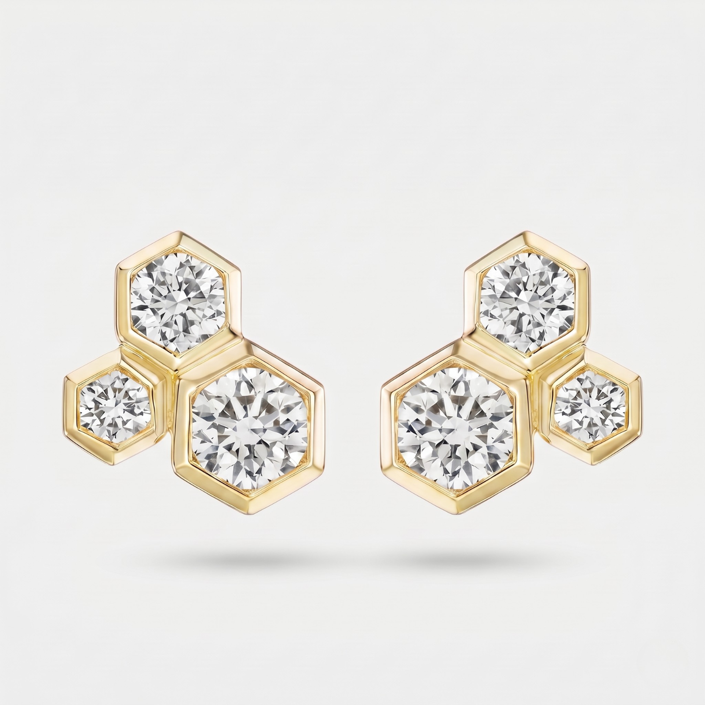 A pair of gold hexagonal stud earrings with round-cut clear gemstones, displayed on a clean light gray background.
