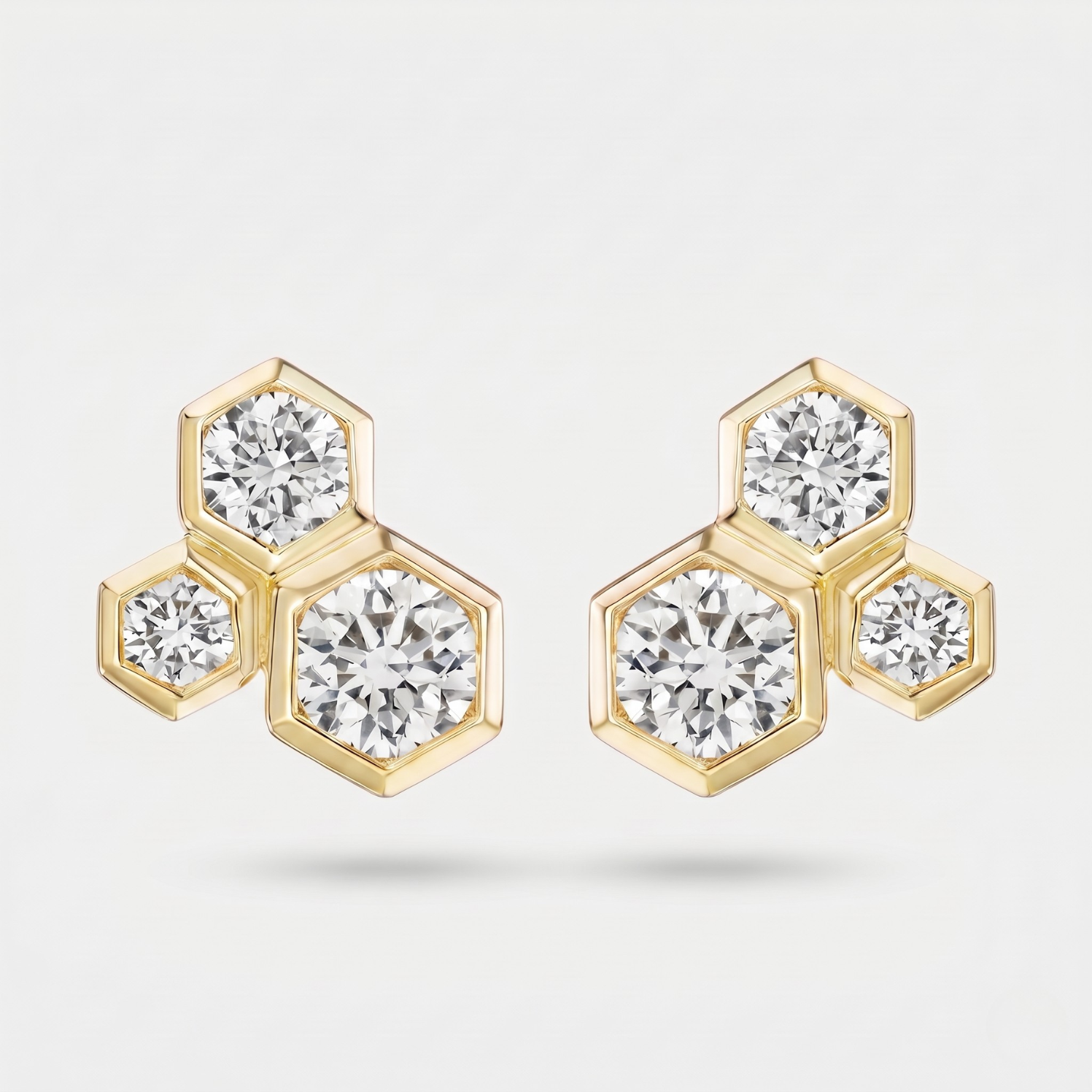 A pair of gold hexagonal stud earrings with round-cut clear gemstones, displayed on a clean light gray background.