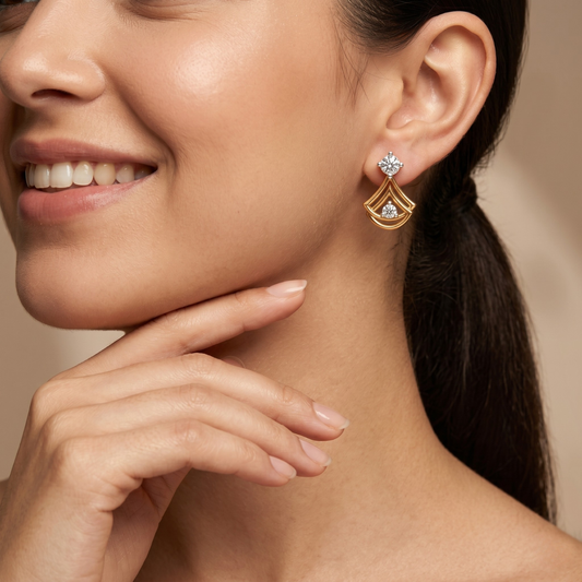 A close-up lifestyle shot of a woman wearing a gold geometric drop earring with clear gemstones, showing the earring on her ear against a warm beige background.