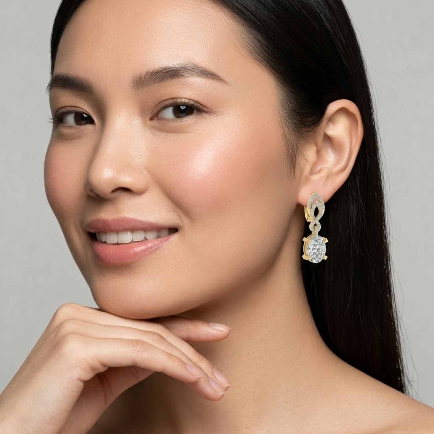 A close-up portrait of a woman wearing a gold drop earring with a clear faceted gemstone, set against a soft light gray background.
